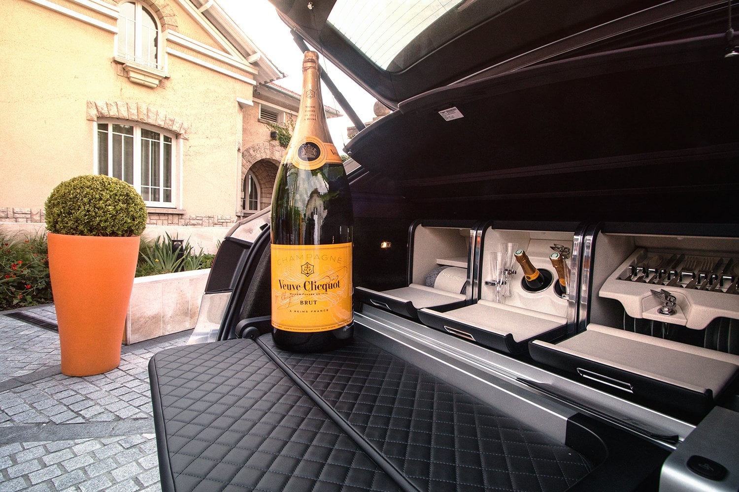 Champagner und Reiseaccessoires im geöffneten Kofferraum eines Luxuswagens