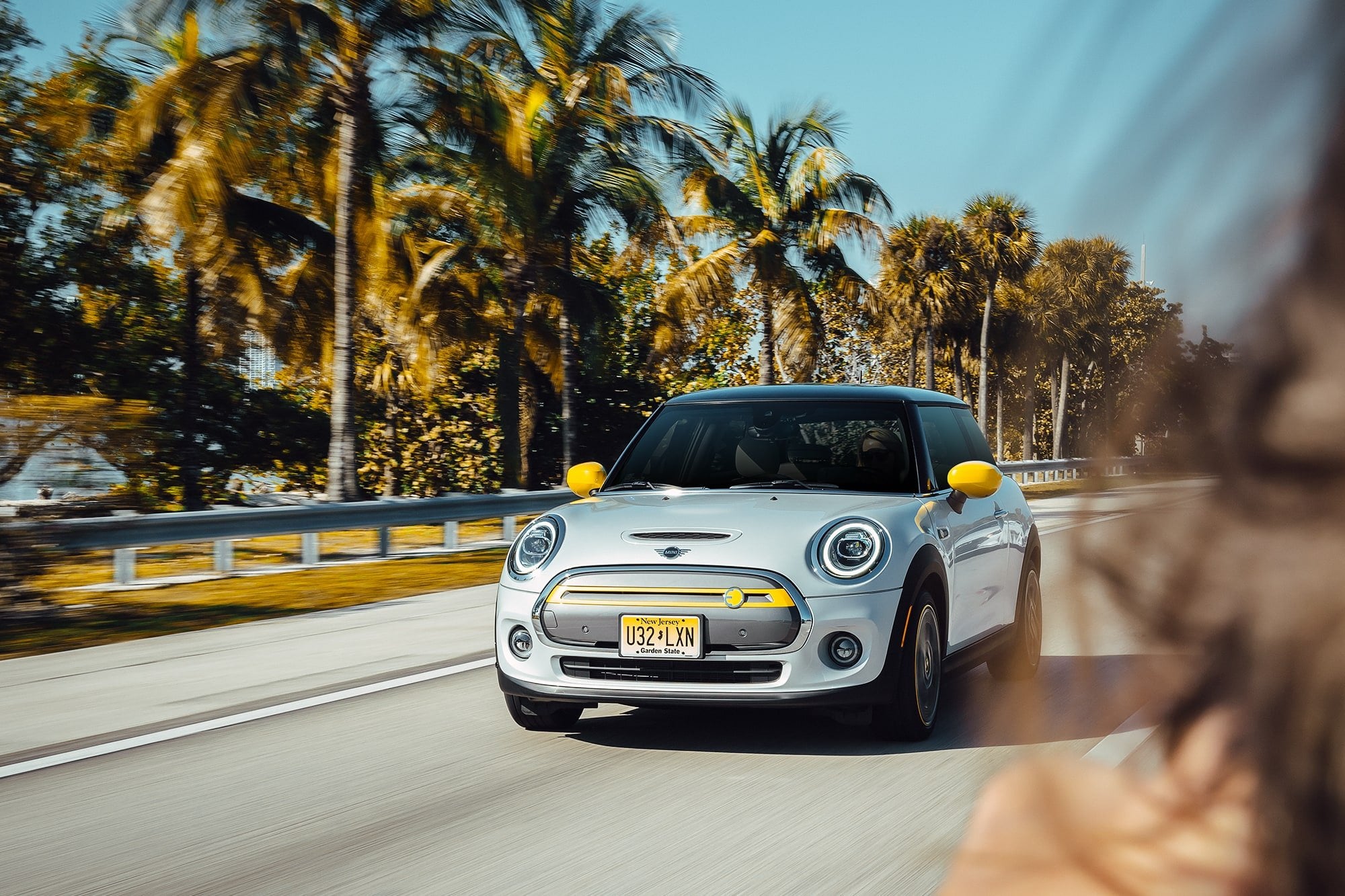 Weißer Mini Cooper auf einer sonnigen Straße zwischen Palmen